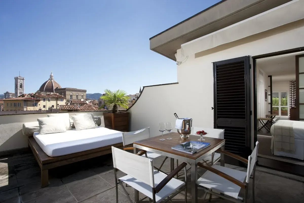On a private rooftop terrace: a portion of the Florence skyline is visible, a day bed awaits travelers and champagne sits on a classy outdoor table