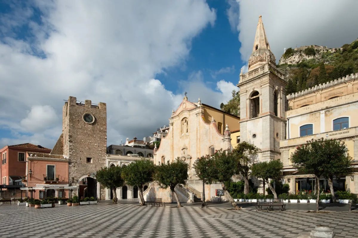 Geometric tiles lead up to a tree garden and historic Sicilian architecture