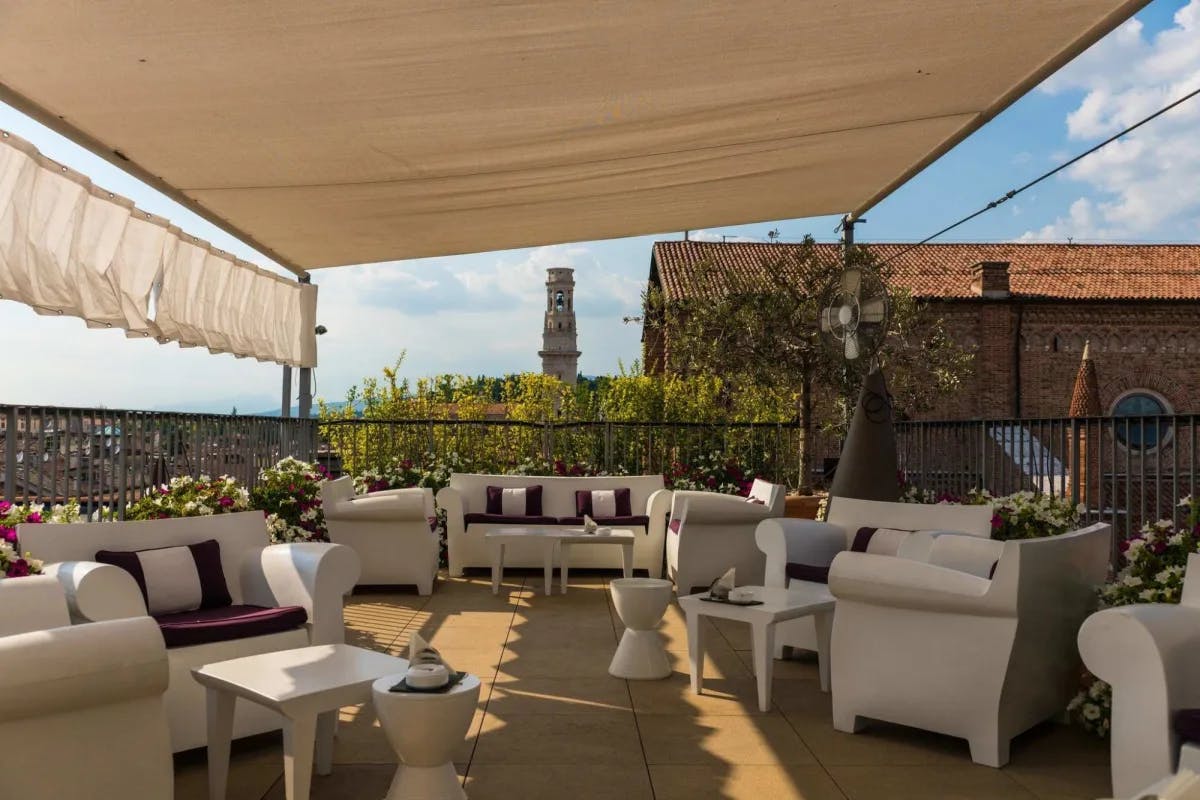 Beneath a rooftop awning: stylish furniture fills a common space while Verona's historic architecture is visible in the distance