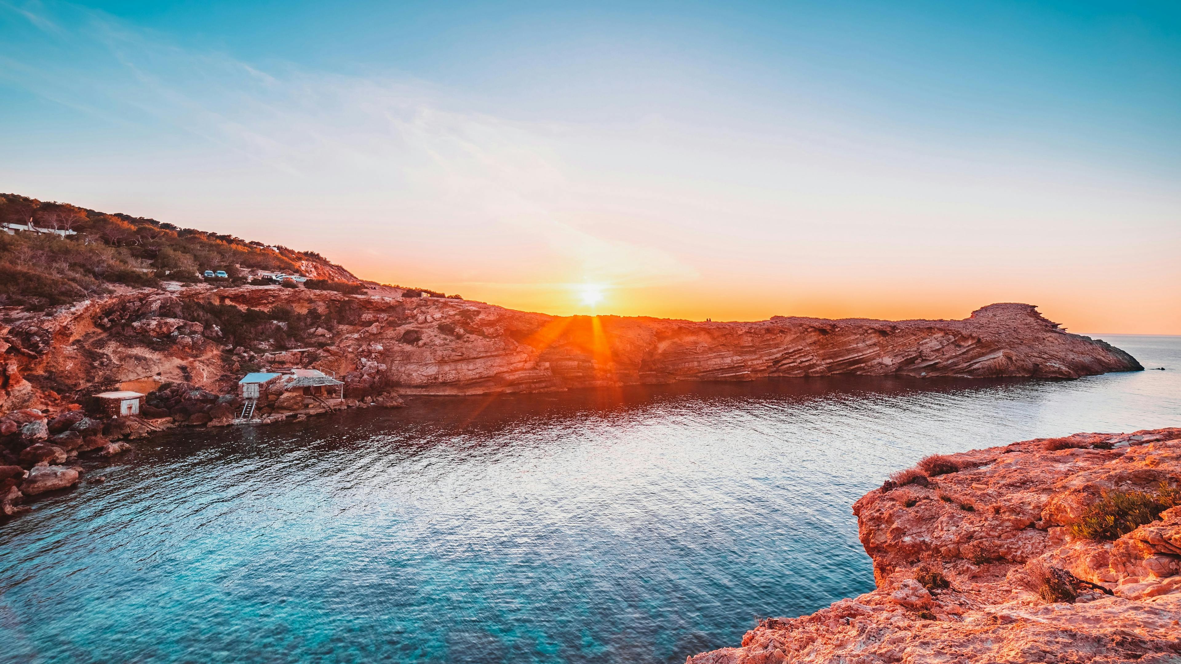 The sun setting over rocks near a bay in Ibiza.